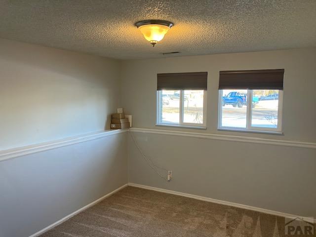 spare room featuring carpet, visible vents, a textured ceiling, and baseboards