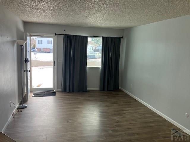 empty room featuring dark wood-style flooring, a textured ceiling, and baseboards