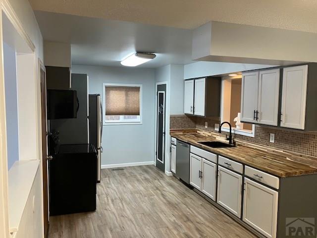 kitchen featuring stainless steel appliances, wooden counters, backsplash, a sink, and light wood-type flooring