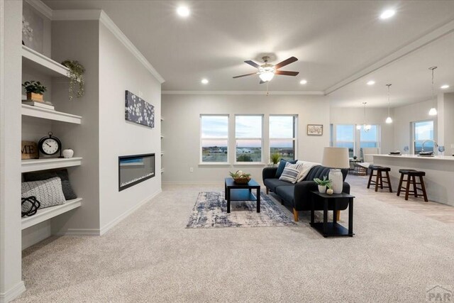 living area with ornamental molding, recessed lighting, a glass covered fireplace, and light colored carpet