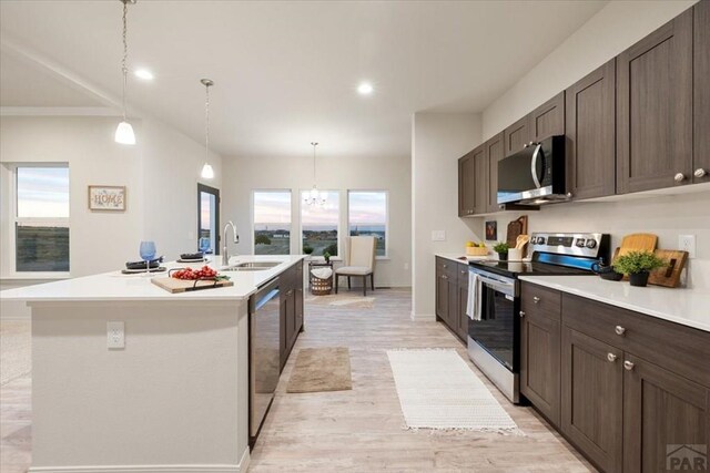 kitchen with a kitchen island with sink, stainless steel appliances, a sink, hanging light fixtures, and light countertops