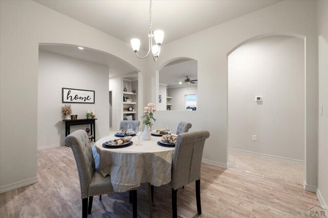 dining room featuring built in shelves, light wood-style floors, baseboards, and ceiling fan with notable chandelier