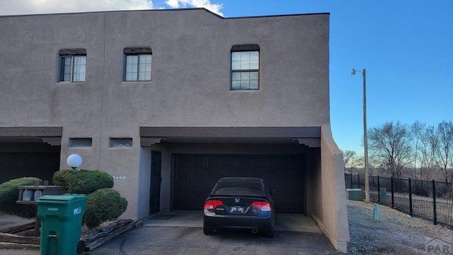 view of front of house with an attached garage, fence, and stucco siding