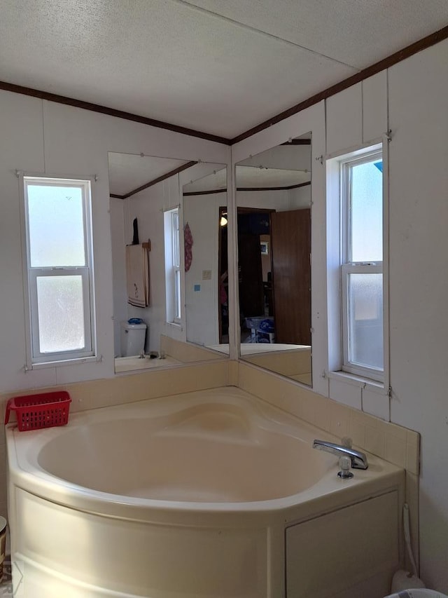 bathroom with a textured ceiling, a bath, and crown molding