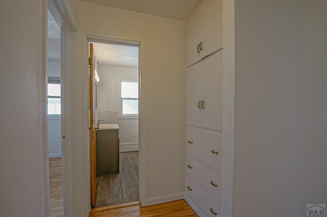 corridor featuring light wood-type flooring and a sink