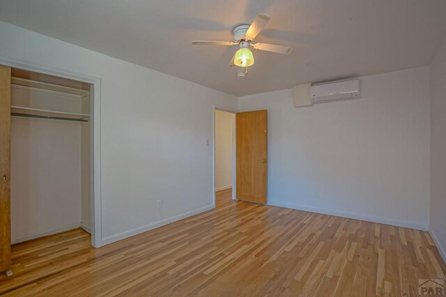 unfurnished bedroom featuring a wall unit AC, light wood finished floors, baseboards, and a closet