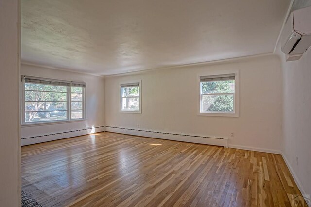 empty room with a wall unit AC, light wood finished floors, baseboards, and a baseboard heating unit