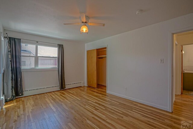 unfurnished bedroom featuring ceiling fan, a baseboard radiator, light wood-style flooring, baseboards, and a closet