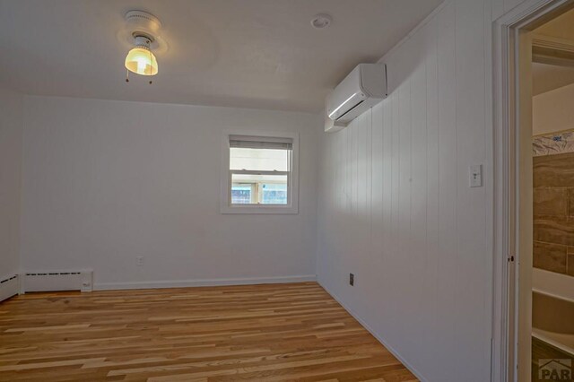 unfurnished room with a wall unit AC, light wood-type flooring, and baseboard heating