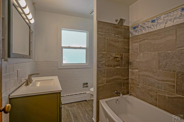 full bathroom with tile walls, toilet, baseboard heating, vanity, and wood finished floors