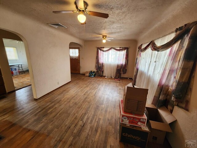 unfurnished room featuring arched walkways, visible vents, a textured wall, a textured ceiling, and wood finished floors