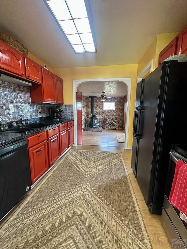 620 S 7th St, Springfield, CO 81073 - kitchen featuring a wood stove, black appliances, light wood-style floors, arched walkways, and dark brown cabinets