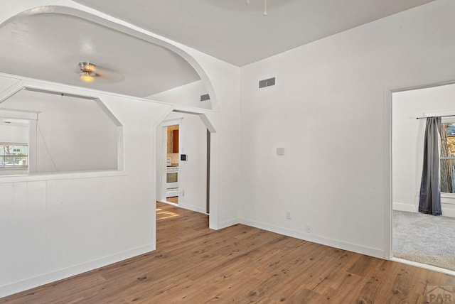 unfurnished room with baseboards, visible vents, arched walkways, and wood finished floors