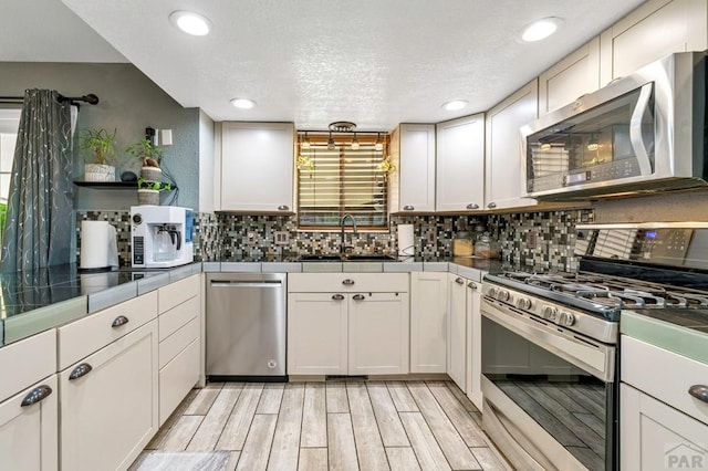 kitchen with tile counters, a sink, wood tiled floor, stainless steel appliances, and backsplash