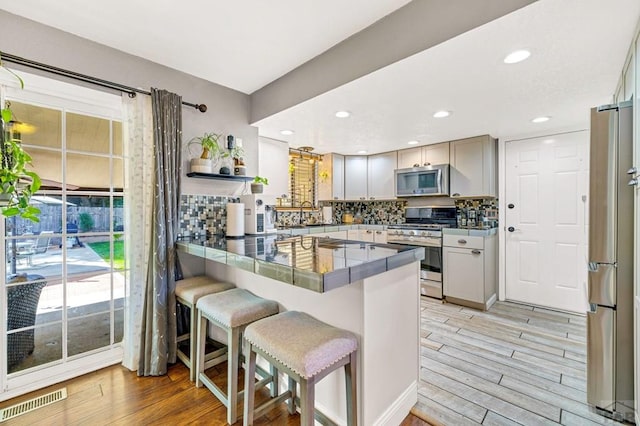 kitchen with visible vents, appliances with stainless steel finishes, light wood-type flooring, a peninsula, and a kitchen breakfast bar