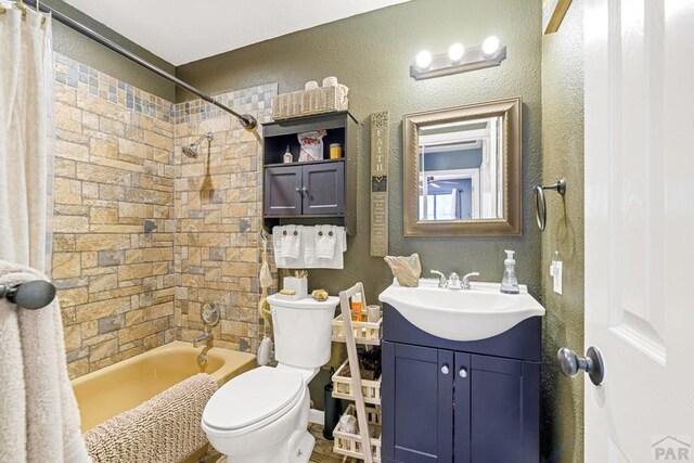 bathroom featuring toilet, a textured wall, shower / bath combo with shower curtain, and vanity