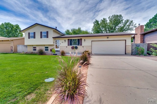 tri-level home featuring brick siding, an attached garage, fence, driveway, and a front lawn