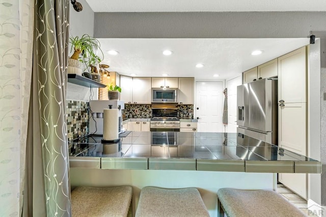 kitchen featuring tile countertops, a breakfast bar area, stainless steel appliances, a peninsula, and decorative backsplash