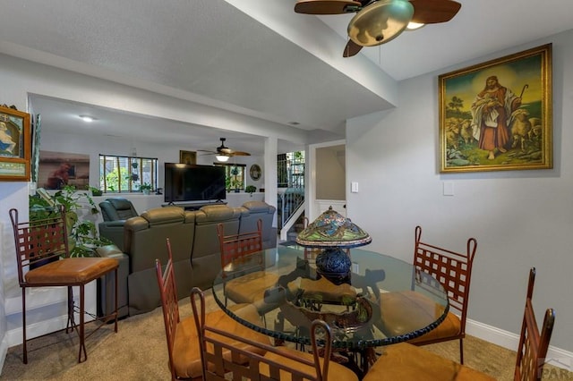 dining room featuring a ceiling fan, light colored carpet, baseboards, and stairs