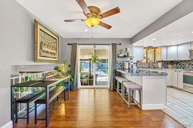 kitchen featuring a breakfast bar area, wood-type flooring, decorative backsplash, appliances with stainless steel finishes, and a peninsula