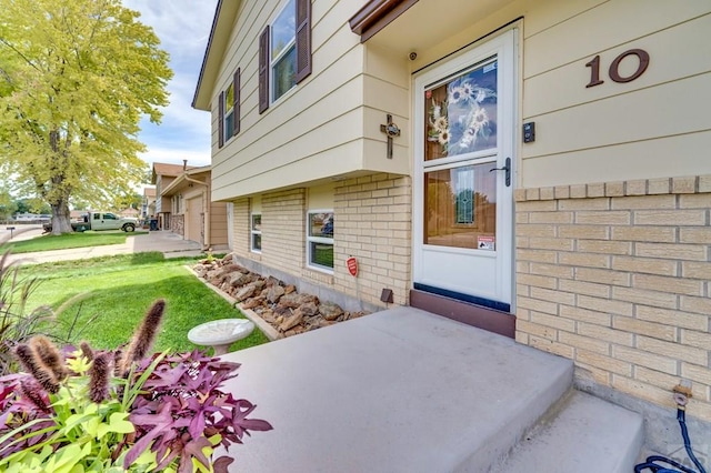 doorway to property with a garage, a yard, and brick siding