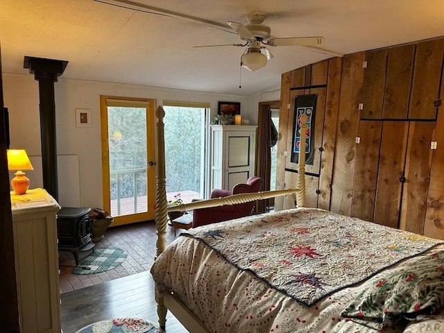 bedroom with access to outside, a wood stove, ceiling fan, and hardwood / wood-style flooring