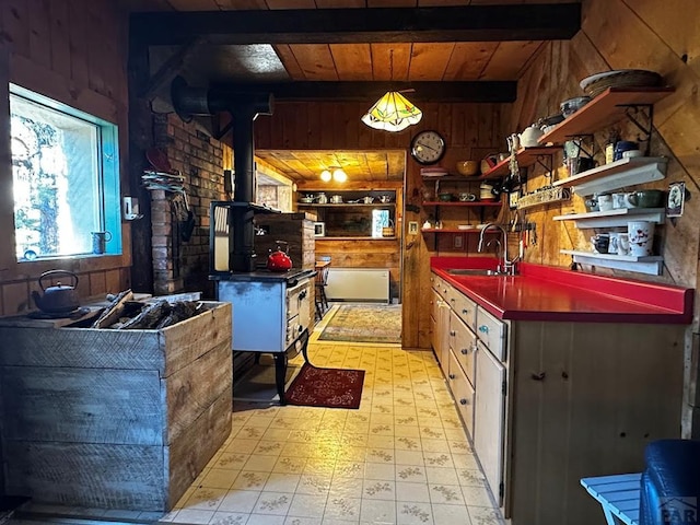 kitchen with dark countertops, beamed ceiling, a wood stove, light floors, and a sink