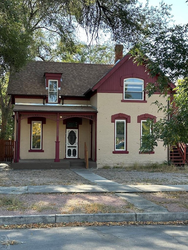 view of front of property with covered porch, brick siding, a chimney, and a shingled roof