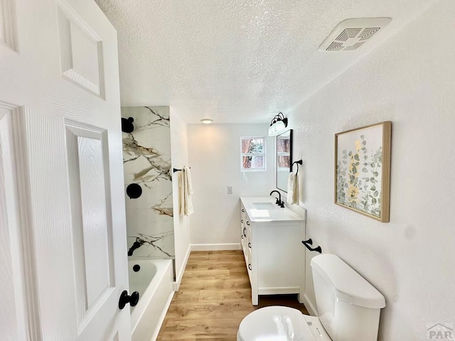 bathroom with visible vents, toilet, a textured ceiling, vanity, and wood finished floors