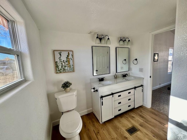 bathroom with double vanity, a sink, toilet, and wood finished floors