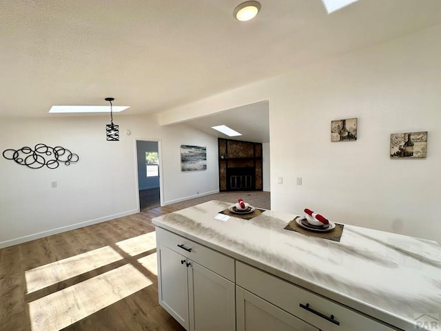 kitchen featuring vaulted ceiling with skylight, baseboards, dark wood finished floors, open floor plan, and pendant lighting