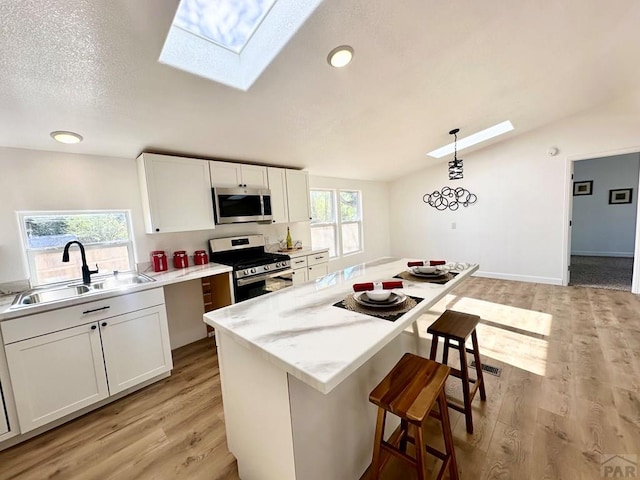 kitchen with a center island, decorative light fixtures, appliances with stainless steel finishes, white cabinetry, and a sink