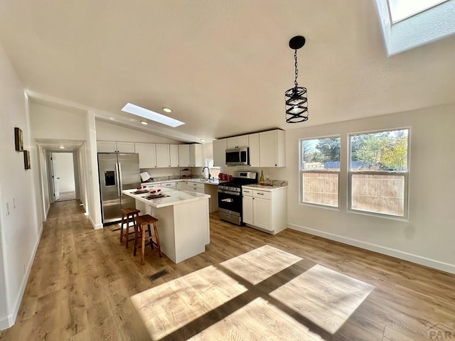 kitchen with a center island, pendant lighting, stainless steel appliances, light countertops, and white cabinetry