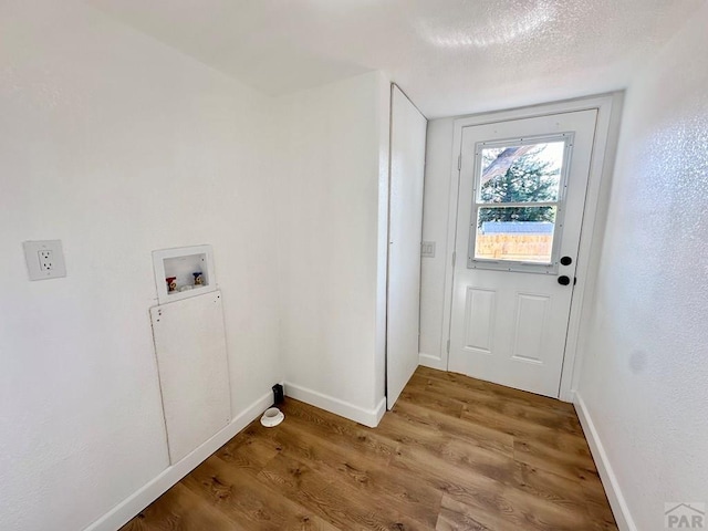 doorway to outside featuring a textured ceiling, baseboards, and wood finished floors