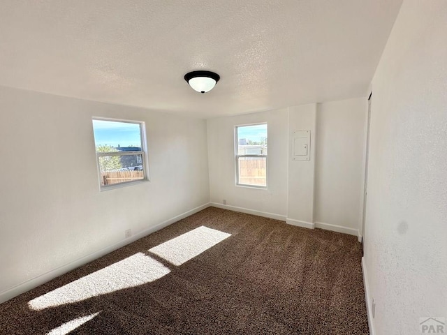 empty room with baseboards, dark colored carpet, and a textured ceiling