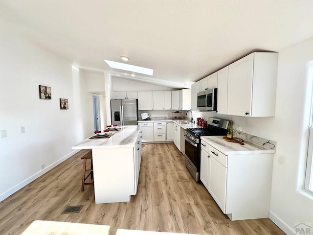 kitchen featuring a center island, a breakfast bar area, light countertops, appliances with stainless steel finishes, and white cabinets