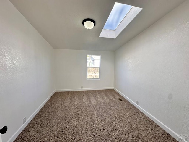 carpeted spare room with vaulted ceiling with skylight, visible vents, and baseboards