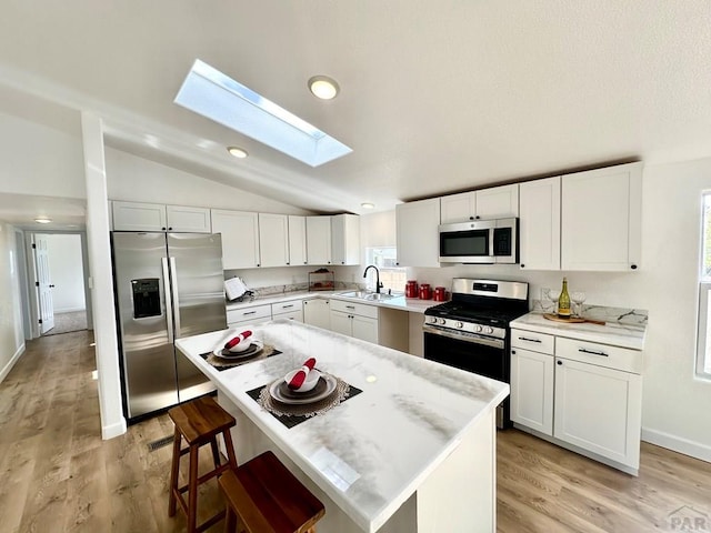 kitchen featuring appliances with stainless steel finishes, light countertops, a kitchen island, and white cabinetry