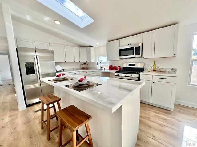 kitchen featuring appliances with stainless steel finishes, a center island, white cabinetry, and a kitchen bar