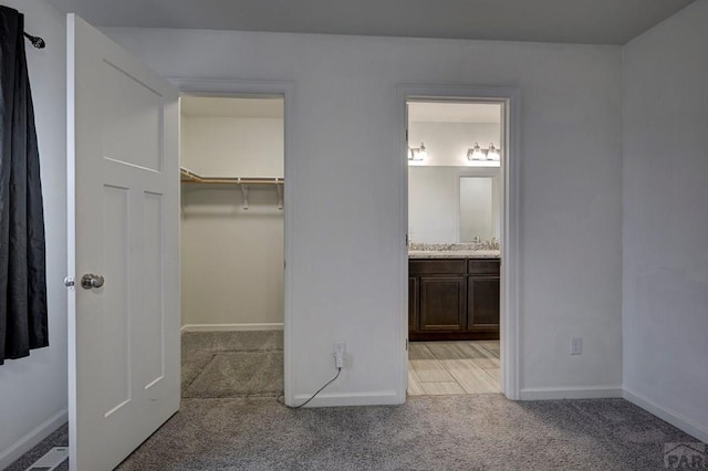 unfurnished bedroom with light carpet, baseboards, visible vents, a walk in closet, and a closet