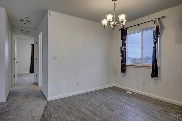 spare room with an inviting chandelier, wood finished floors, visible vents, and baseboards