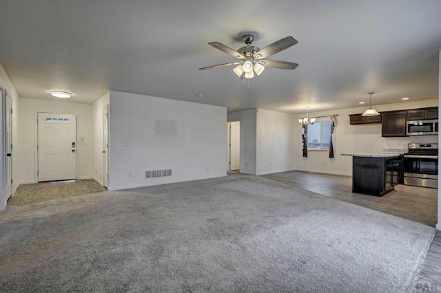 unfurnished living room featuring ceiling fan with notable chandelier, carpet floors, visible vents, and baseboards