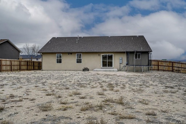 back of property with a fenced backyard, a trampoline, and stucco siding