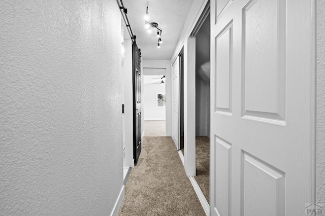 corridor with rail lighting, carpet, a textured ceiling, a barn door, and a textured wall