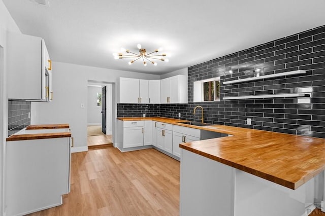 kitchen featuring a sink, backsplash, wooden counters, and a peninsula