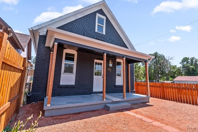view of front of house with brick siding, fence, and covered porch
