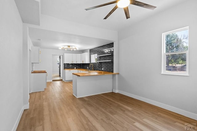 kitchen featuring white cabinets, a sink, a ceiling fan, a peninsula, and decorative backsplash