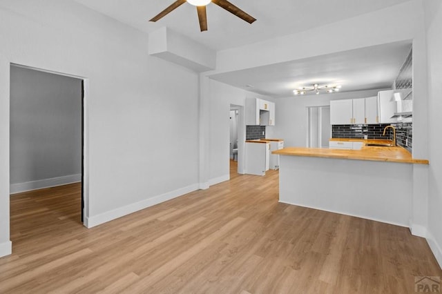 kitchen featuring white cabinets, a sink, a ceiling fan, wood counters, and decorative backsplash