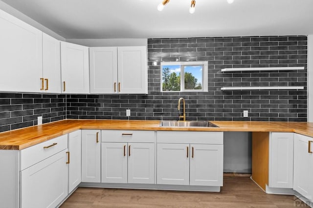 kitchen with light wood-style flooring, wood counters, a sink, and backsplash