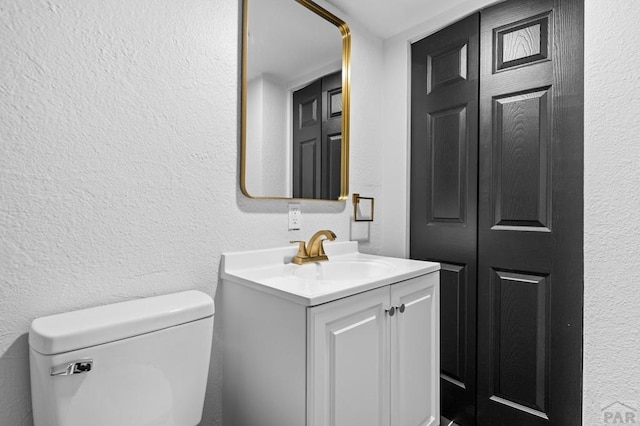 half bath with toilet, vanity, and a textured wall